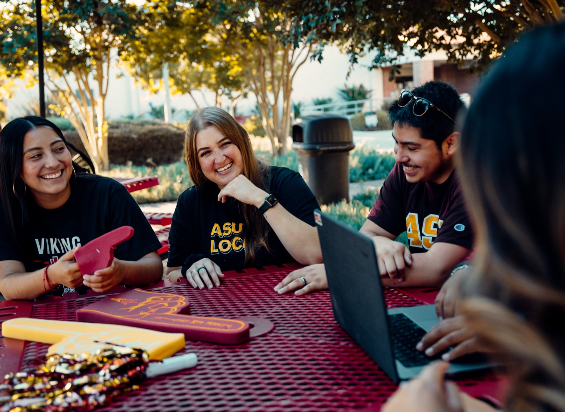 Students wearing ASU Local shirts laugh and work together at an outdoor table, representing the supportive community in Long Beach.