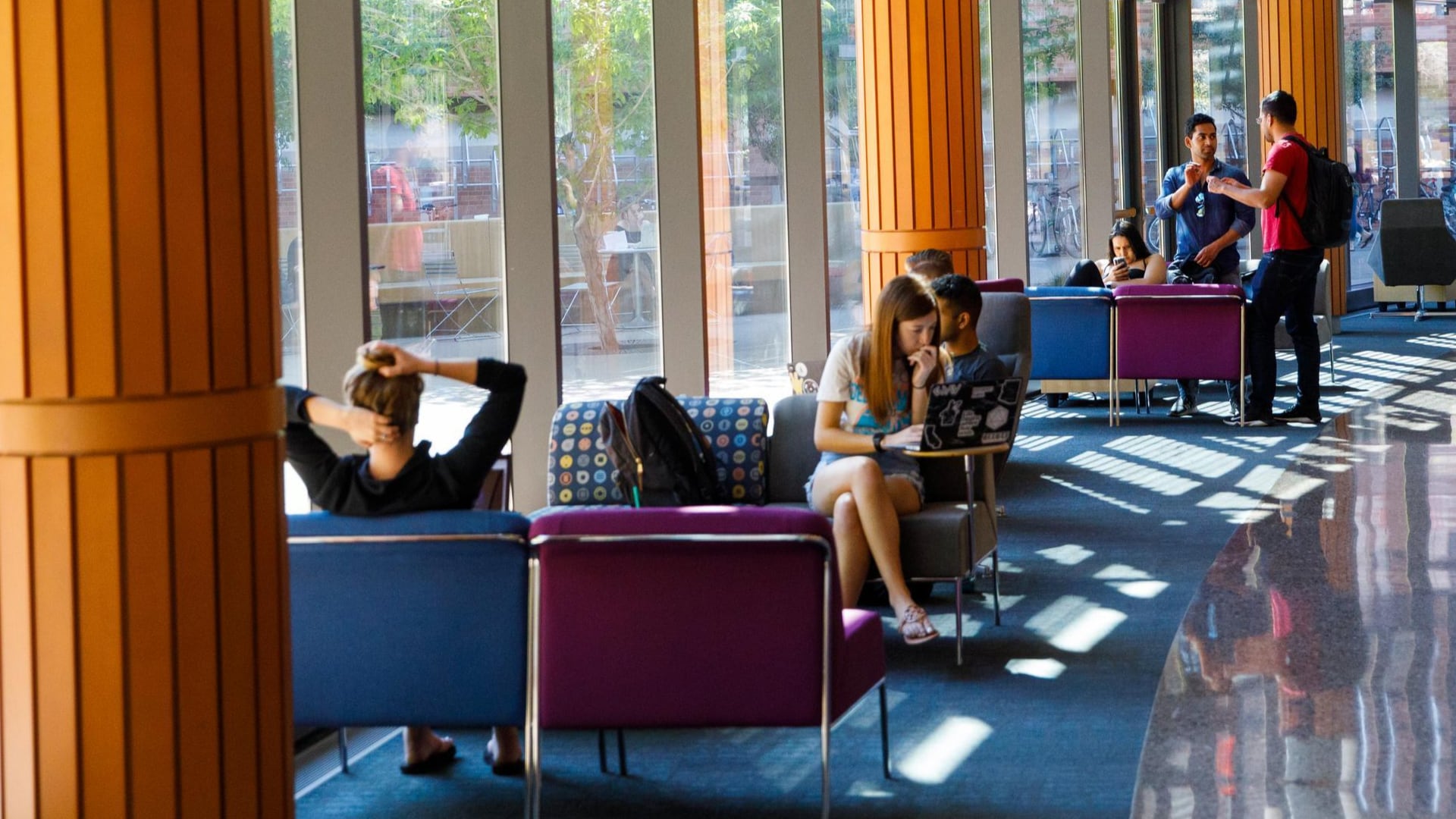 Students study and relax in a bright campus lounge with large windows and colorful seating, highlighting the Study Hall path to earning college credits.